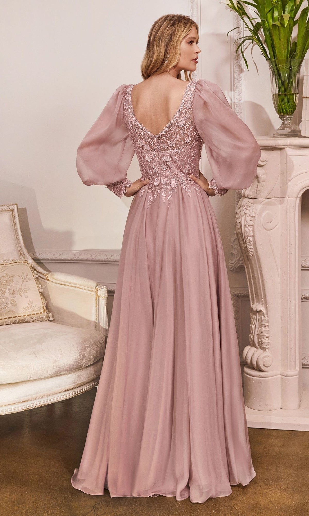 A woman stands indoors facing away from the camera, wearing the Ladivine CD0183 Modest Long Sleeve Formal Gown in mauve with lace bodice detailing and puffed sheer sleeves.